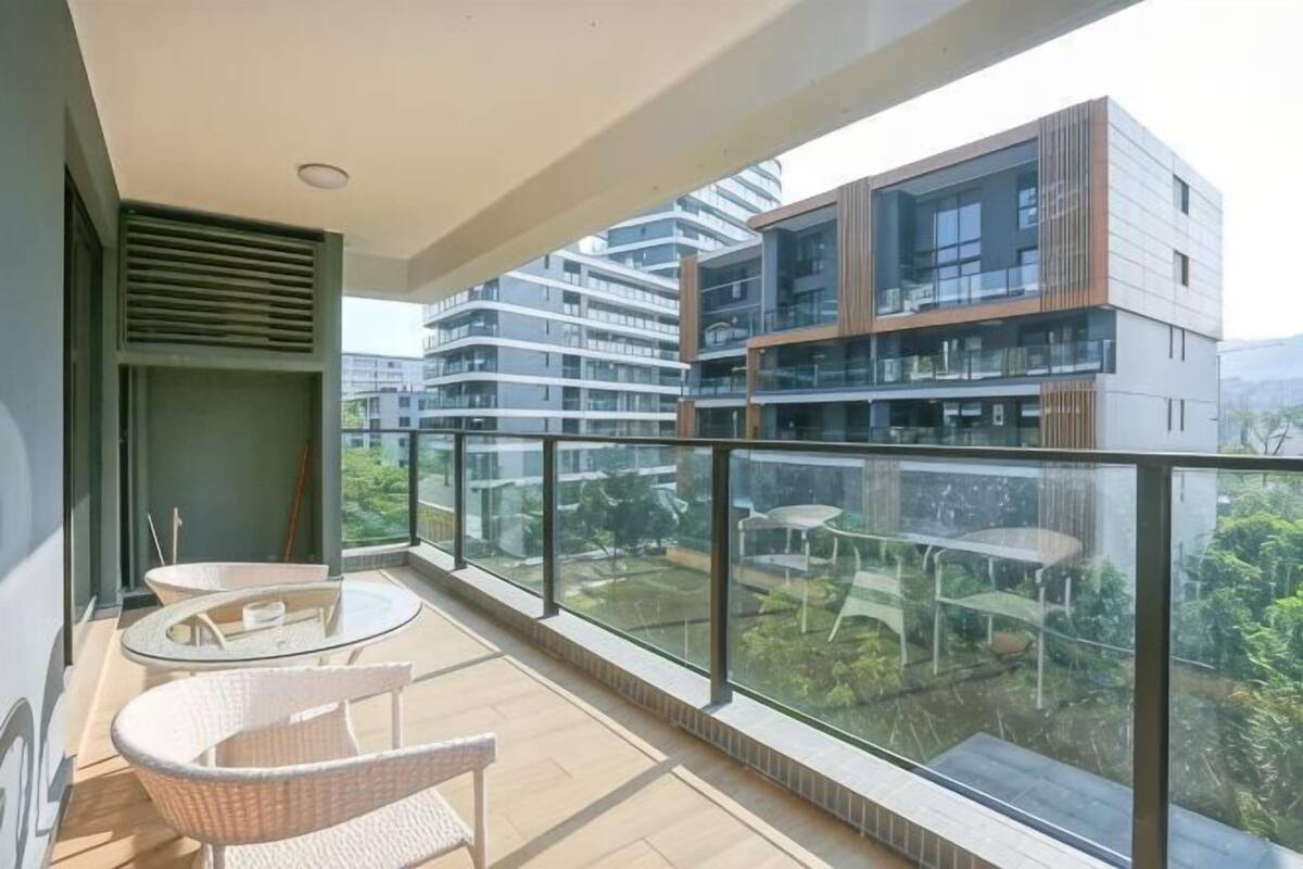 A balcony with wicker chairs, a glass railing, and a view of modern buildings.