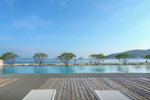 A wooden deck with lounge chairs overlooking a swimming pool and a clear view of the sea.