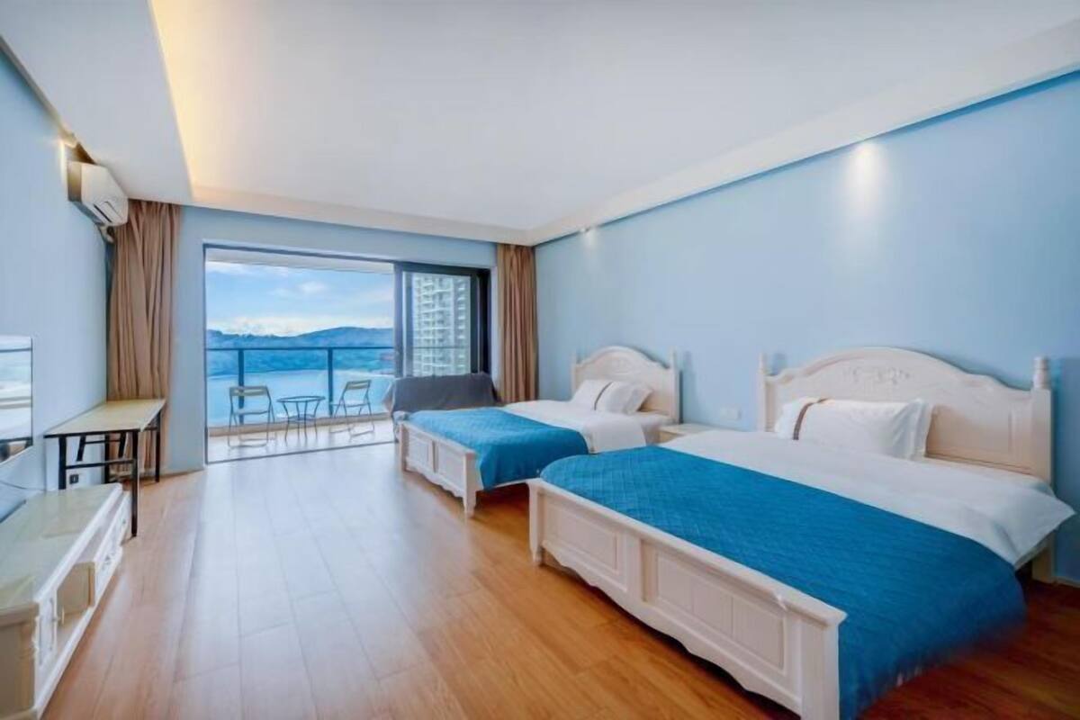 A hotel room with two beds, a desk, and a balcony with a view.