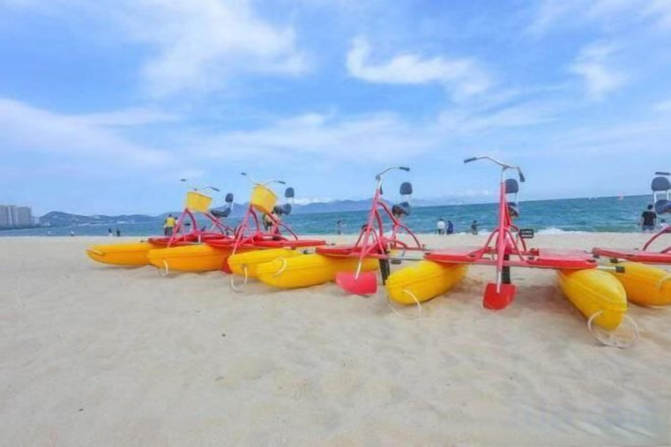 A beach with yellow inflatable kayaks and red paddleboards lined up on the sand.