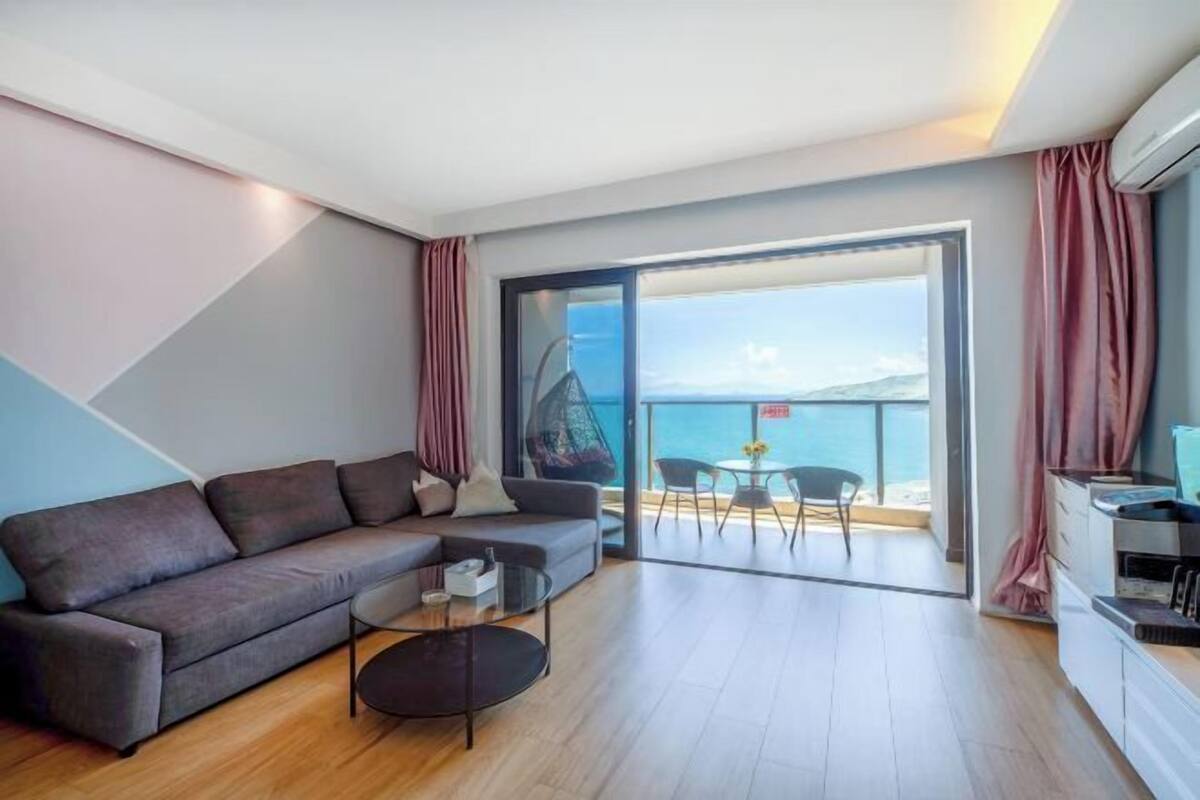 A modern living room with a sofa, coffee table, and a balcony with a view of the sea.