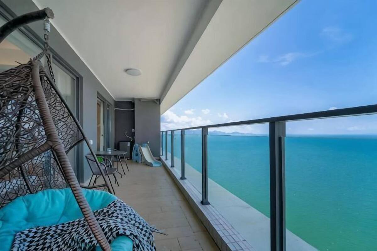 A balcony with a swing chair, a table, and a view of the ocean.