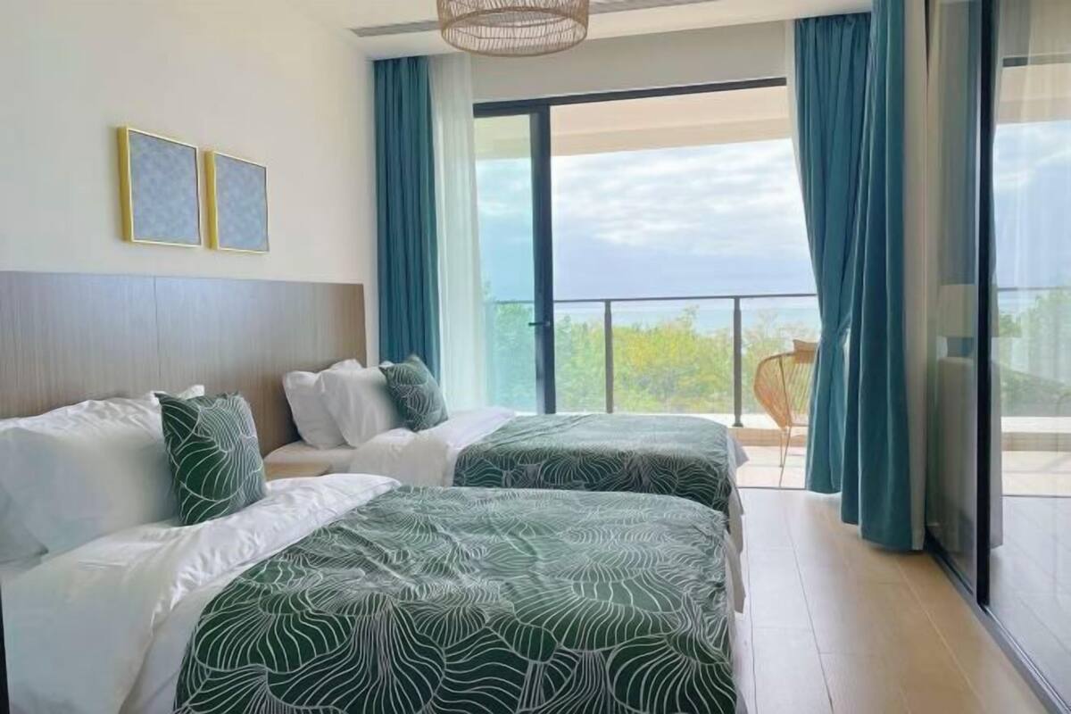 A hotel room with two beds, a balcony with a view, and a large window.