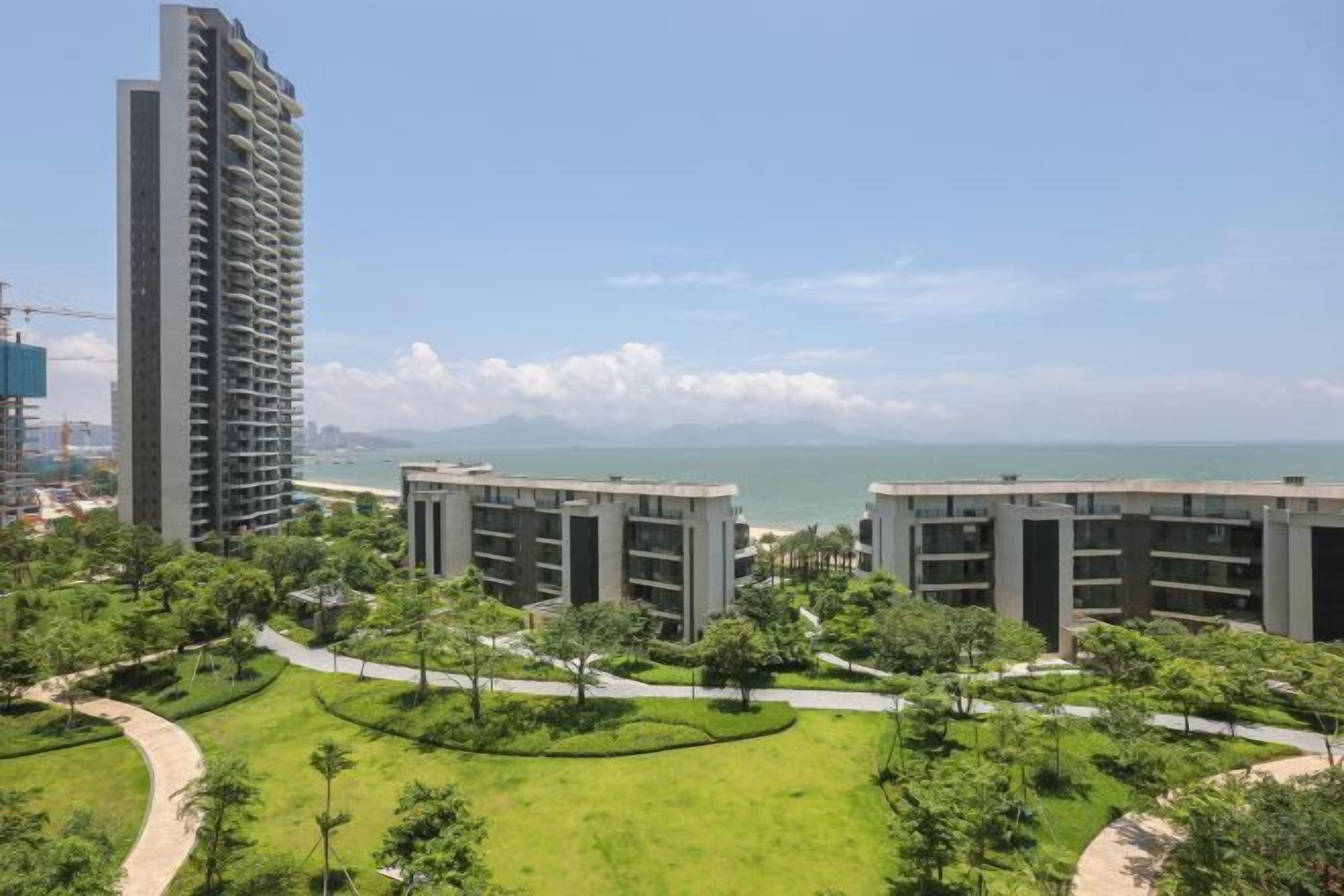 A high-rise building with a view of the sea and a landscaped area with pathways.