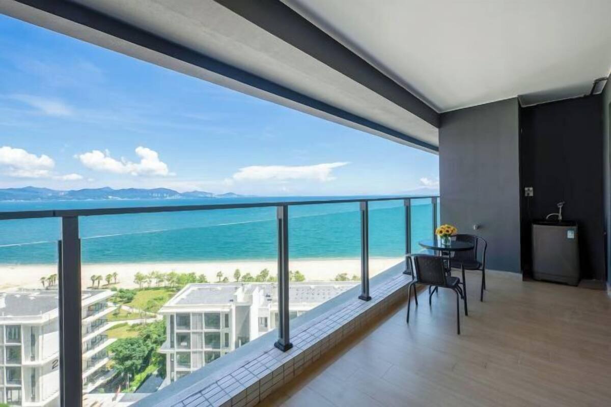 A balcony with a view of the beach and ocean, a table with chairs, and a small kitchen area.