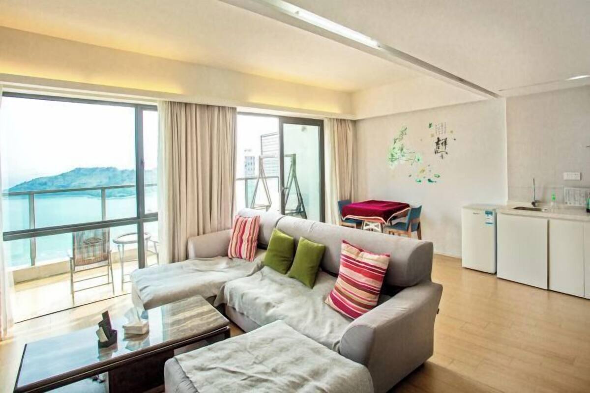 A modern living room with a sofa set, a glass coffee table, and a view of the sea.