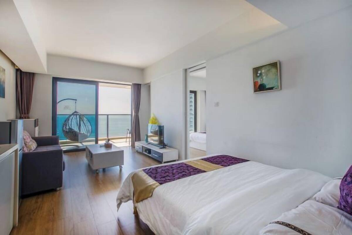 A modern hotel room with a large bed, a balcony with a view, a desk, and a chair.