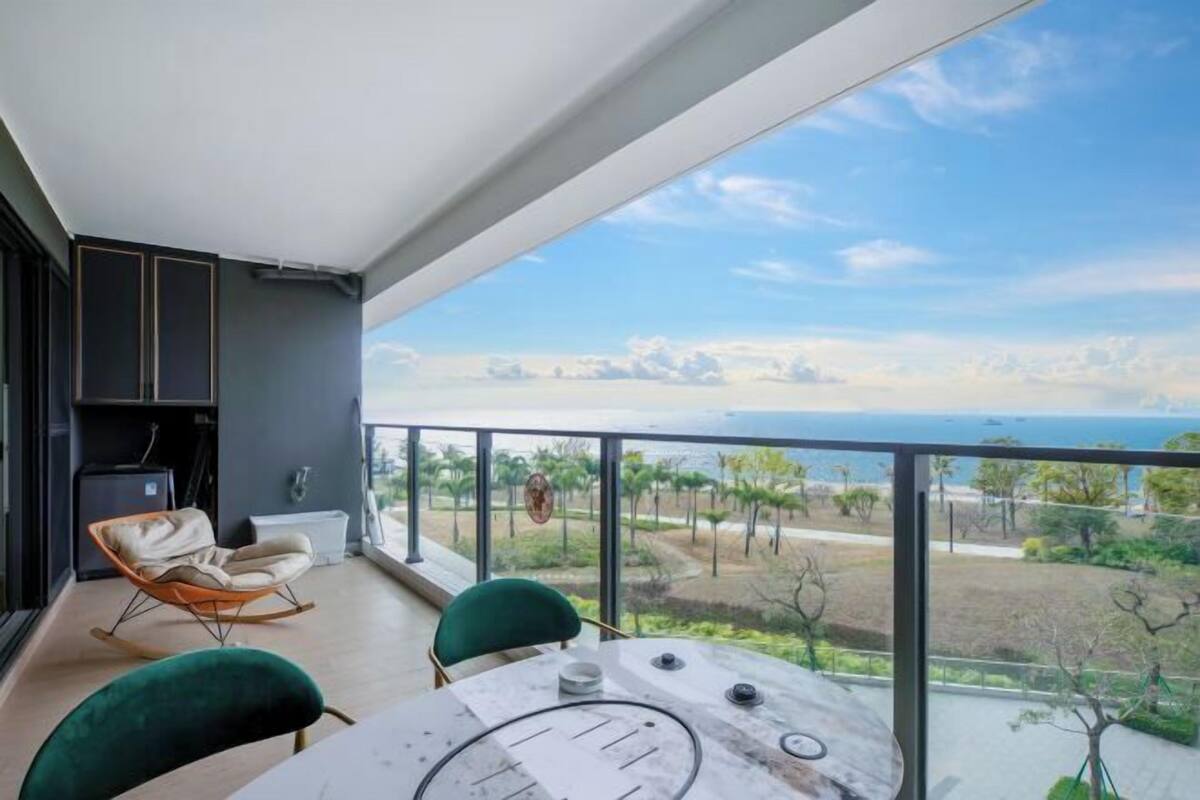 A balcony with a table and chairs, a sofa, and a view of the ocean and landscape.