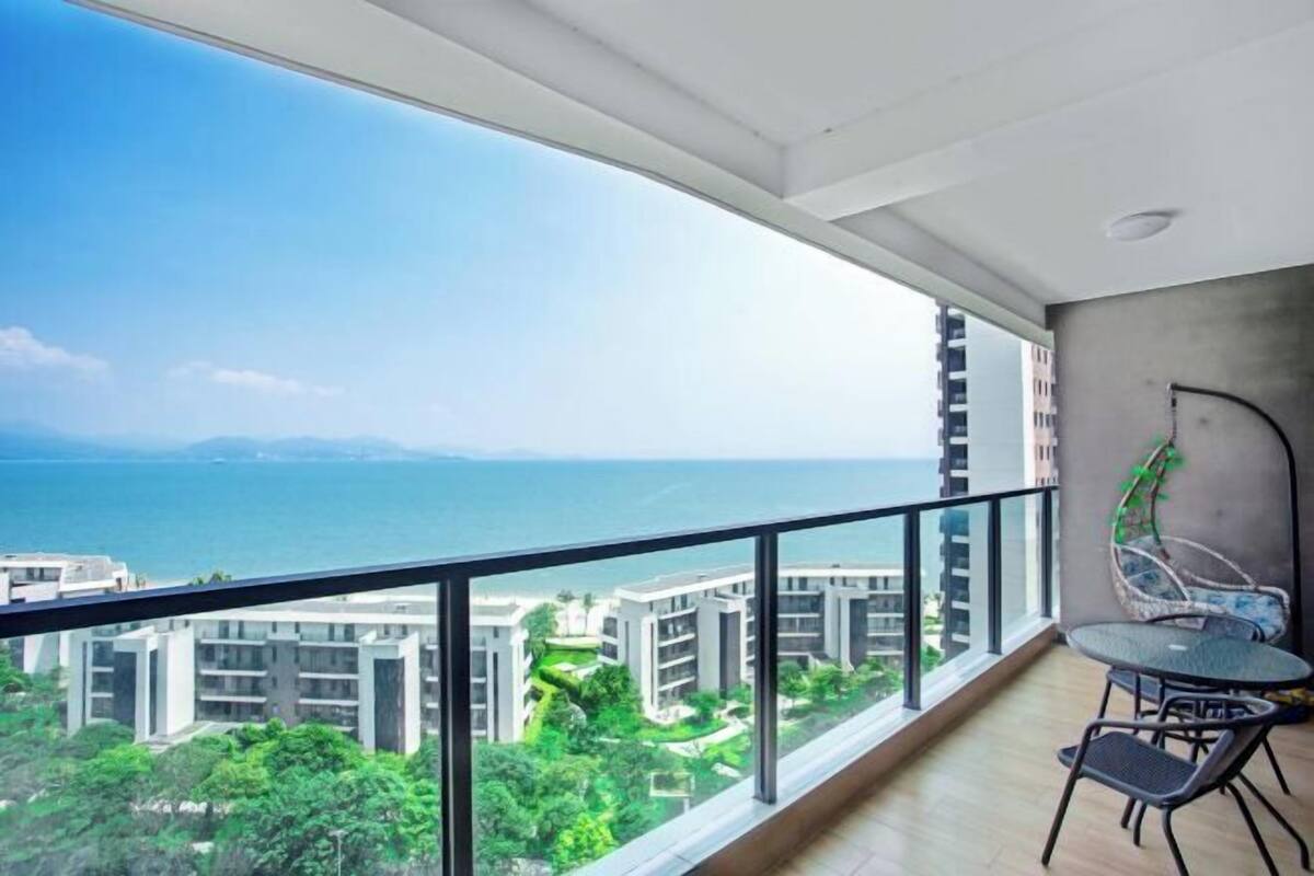 A balcony with a view of a coastal cityscape, a dining table with chairs, and a modern interior design.