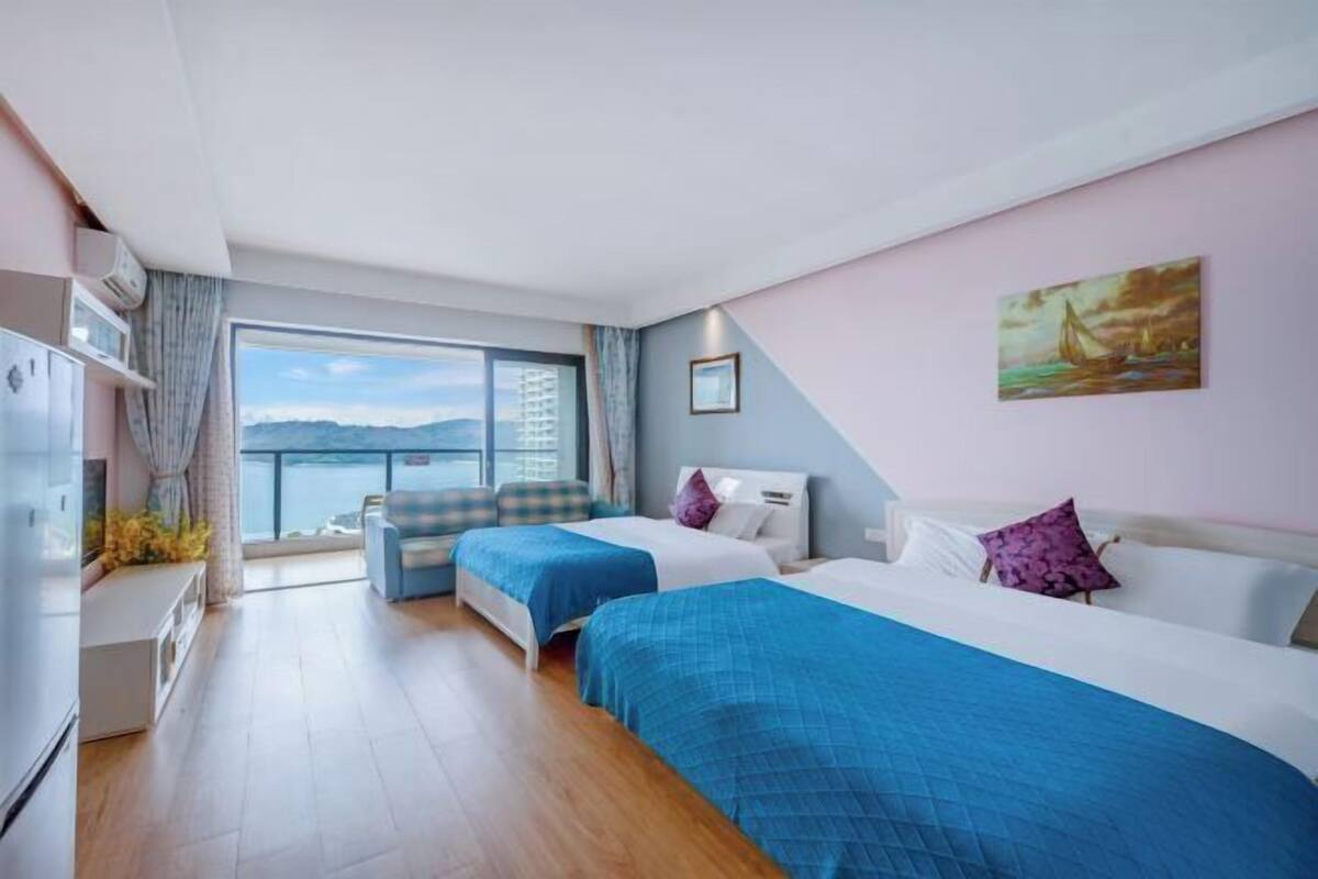 A hotel room with two beds, a large window with a view, a kitchenette, and a painting on the wall.