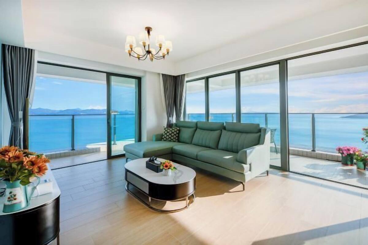 A modern living room with a large sofa, a coffee table, and a view of the sea.