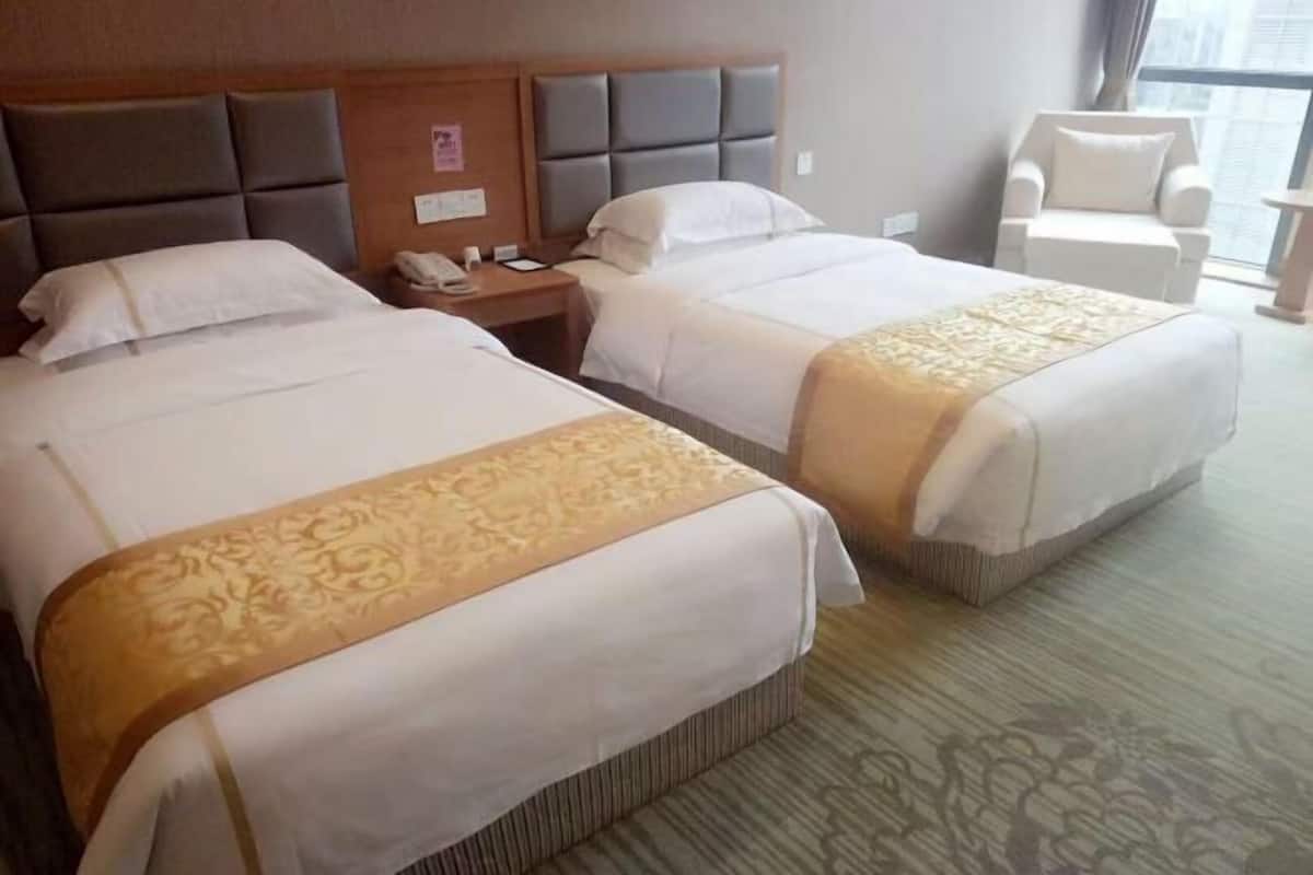 Une chambre d’hôtel avec deux lits, une tête de lit en bois, un téléphone et une chaise.