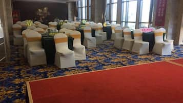 A room with rows of chairs with white covers and orange sashes, a red carpet, and a patterned carpet.