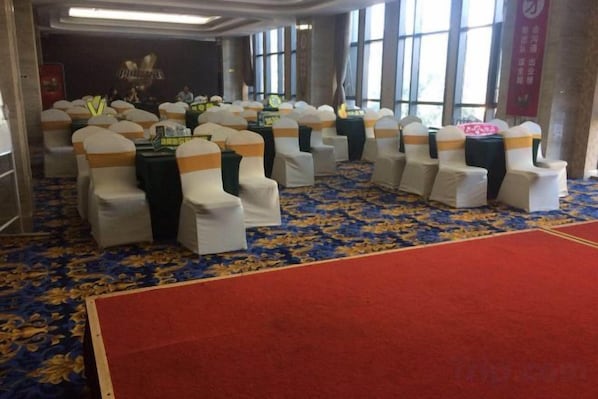 A room with rows of chairs with white covers and orange sashes, a red carpet, and a patterned carpet. - Huaxi Garden Hotel (Qingdao Liuting Airport) (Qingdao)