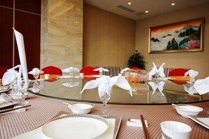Una mesa de comedor lista para una comida, con cubierta de vidrio, mantel blanco y servilletas rojas.