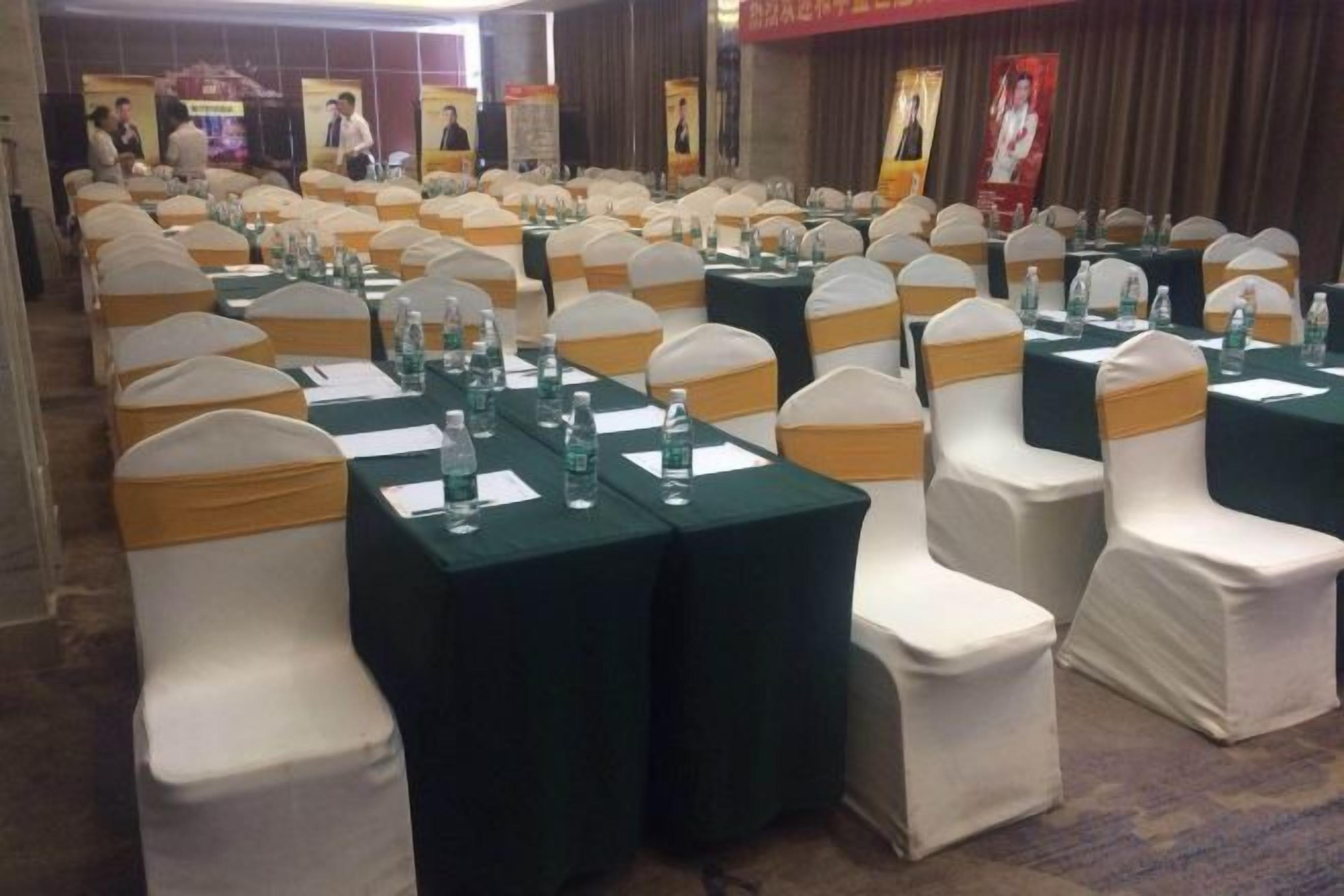 A banquet hall with rows of tables and chairs, each with a green tablecloth and white chair covers.