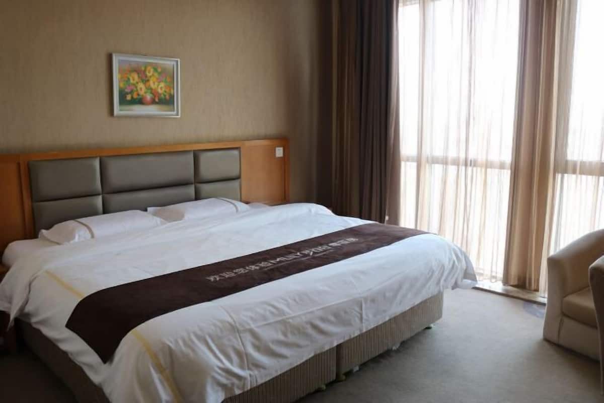 Une chambre d’hôtel avec un lit, une tête de lit, un tableau au mur et une fenêtre avec des rideaux.