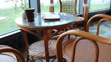 Una mesa con cubierta de vidrio, un cuaderno y una taza, rodeada de sillas de mimbre.