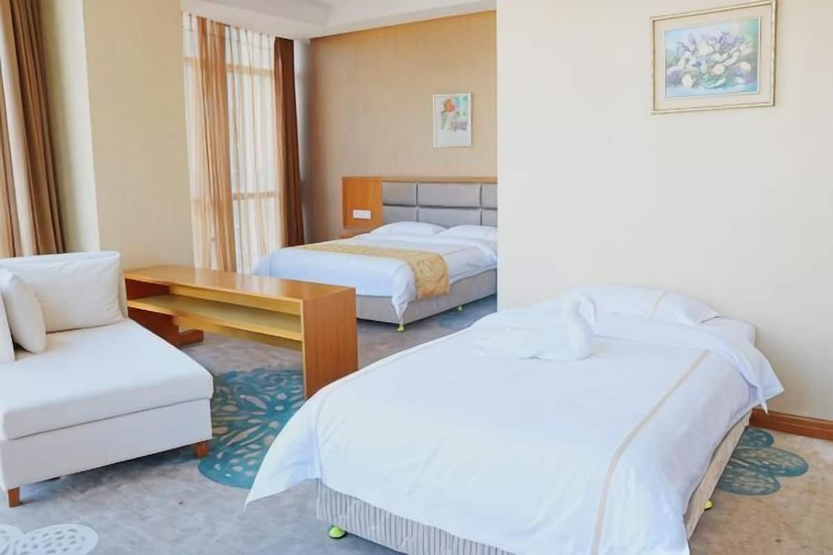 Une chambre d’hôtel avec deux lits, un canapé, une table en bois et une fenêtre avec des rideaux.