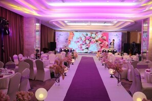 Ein Festsaal mit runden Tischen und einer Bühne, dekoriert mit Blumen und einem Blumenschmuck.