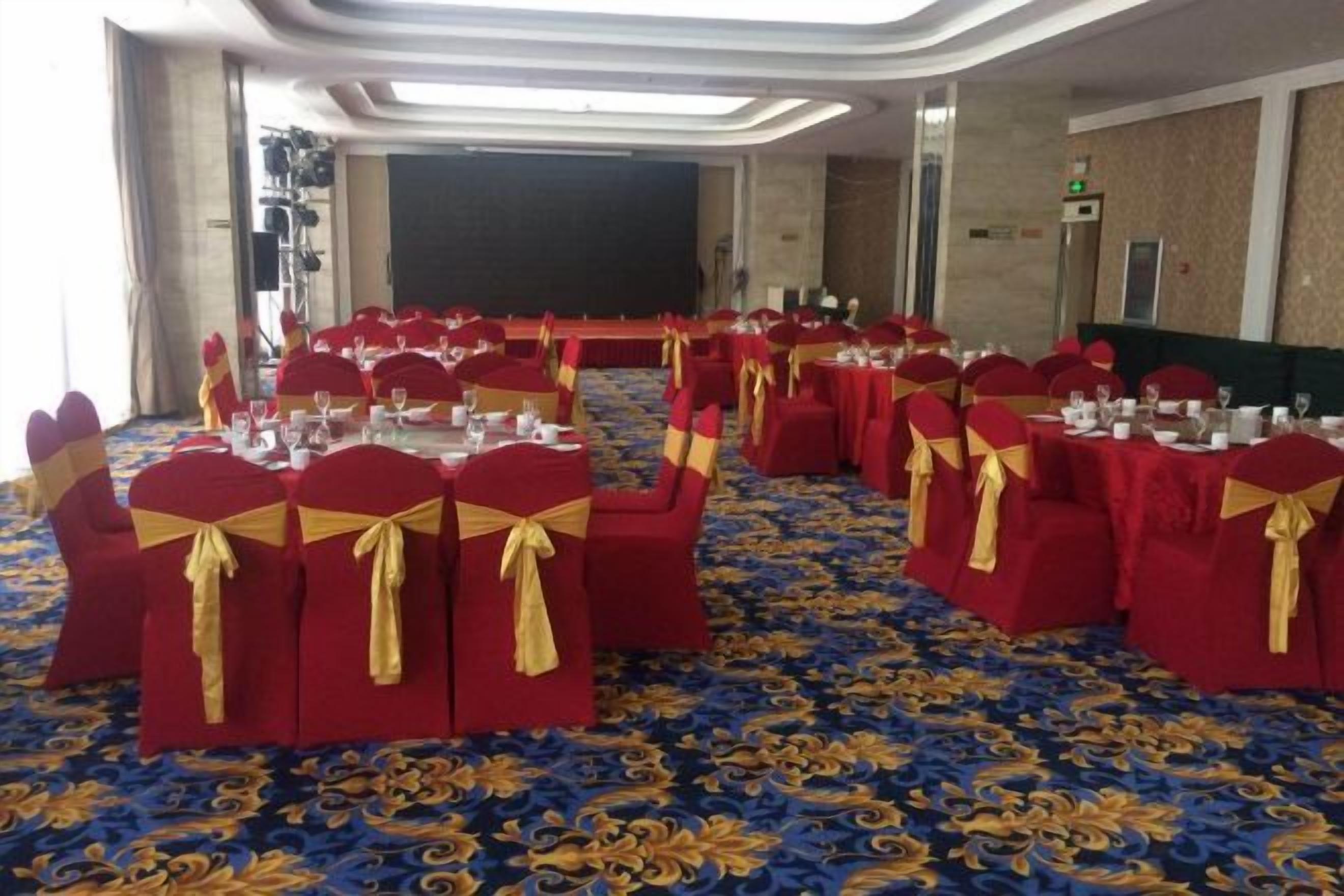 A banquet hall with round tables, red tablecloths, and gold sashes.