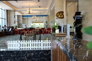 Un hall de hotel con mostrador de recepción, zona de estar y comedor.