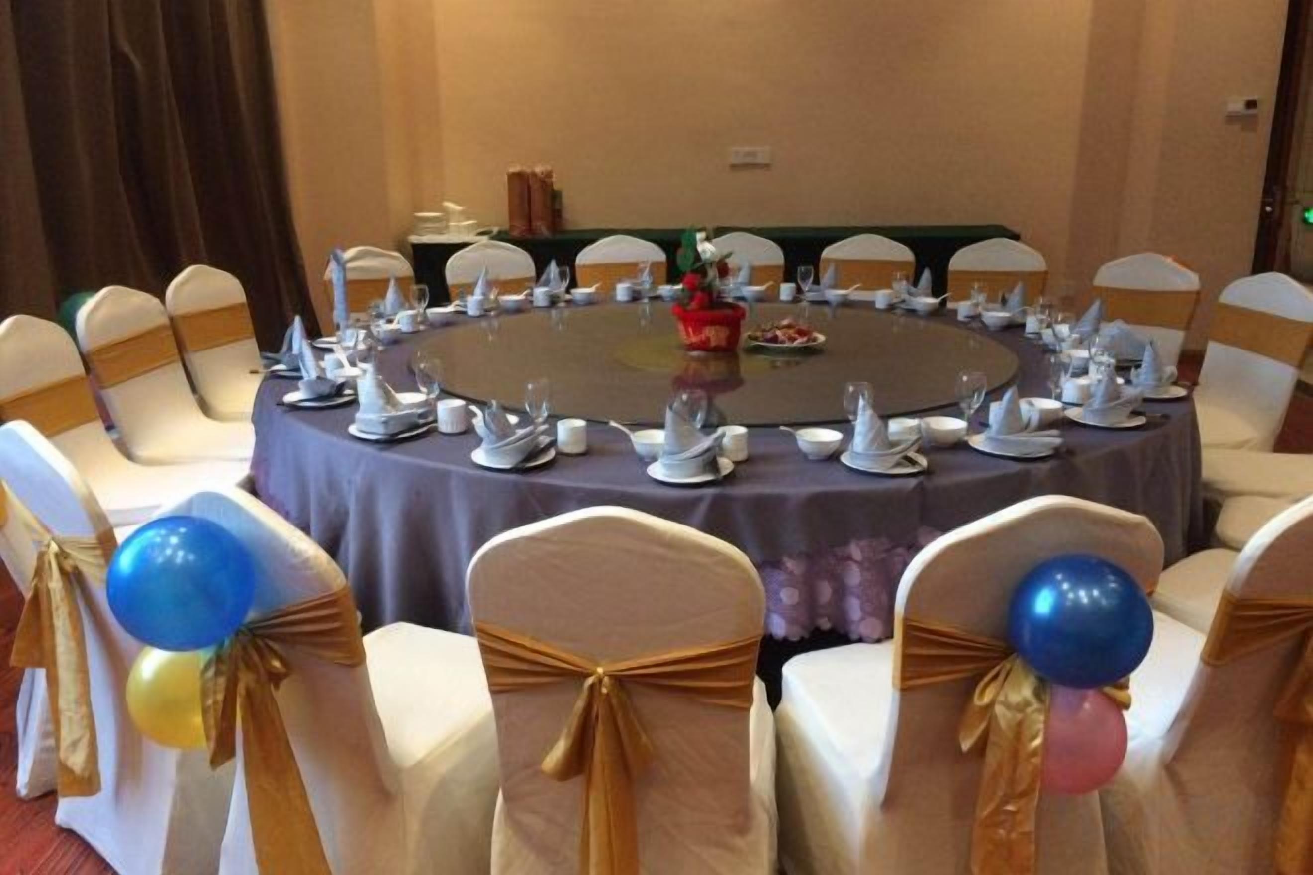 Une table ronde préparée pour une réunion, avec des chaises disposées autour, une nappe et un vase rempli de fleurs.