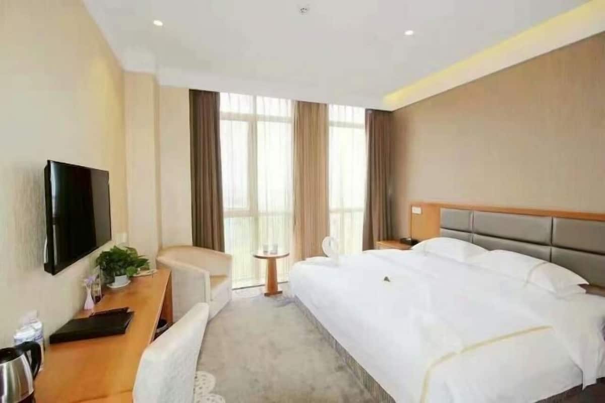 Une chambre d’hôtel avec un lit, une télévision, un bureau agrémenté d’une plante, une chaise et une petite table.