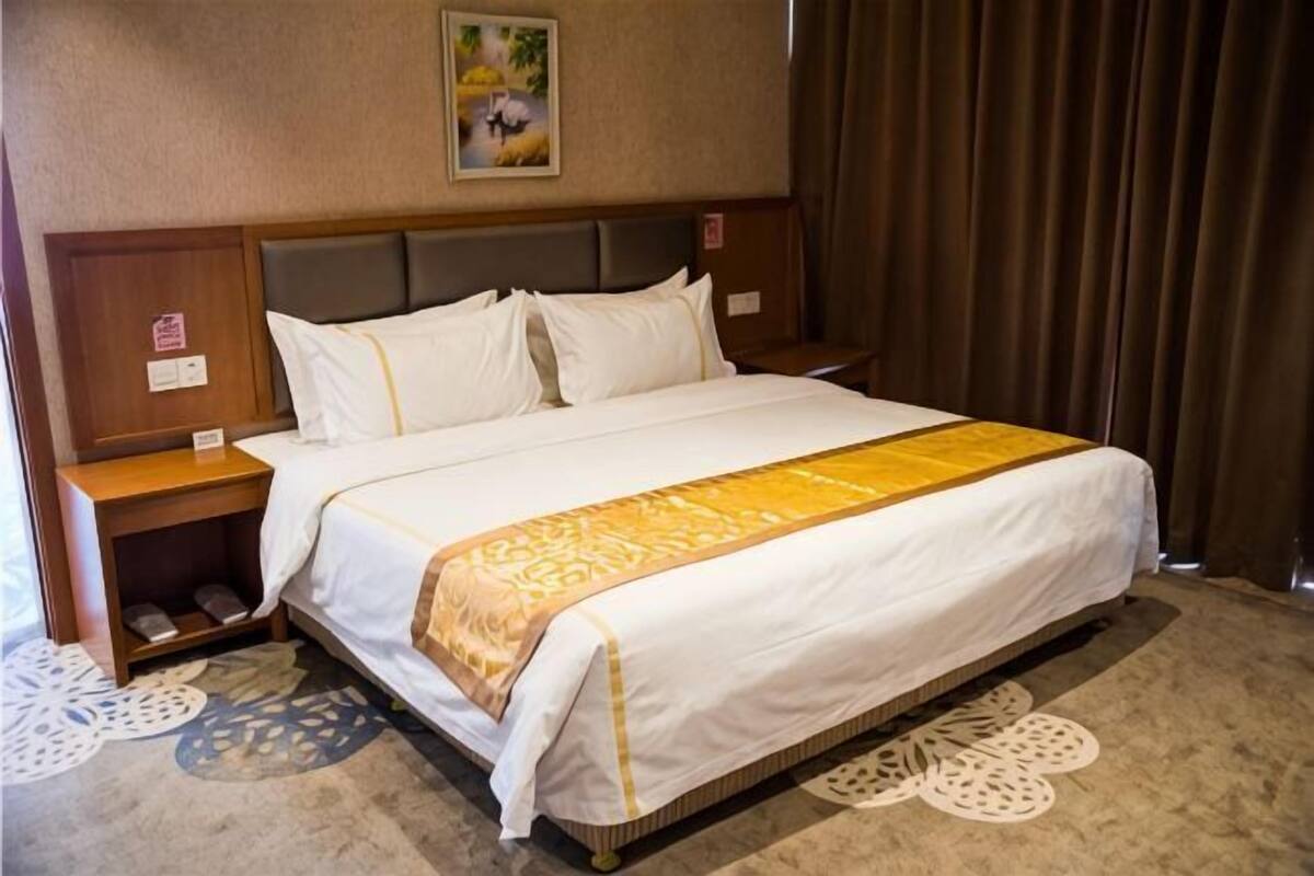 Une chambre d’hôtel comprenant un lit, des tables de chevet, une tête de lit, une moquette à motifs circulaires et un tableau au mur.