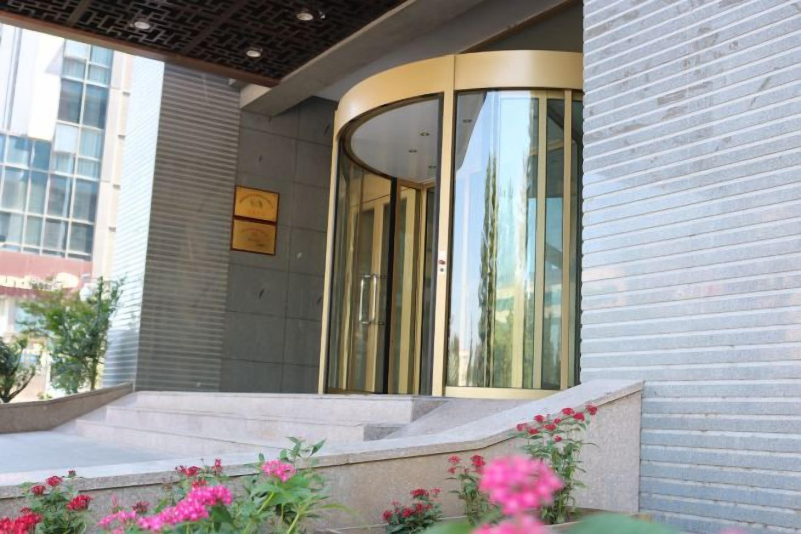 Entrada de un hotel con puerta de vidrio curva, una placa y escalones que conducen a ella.