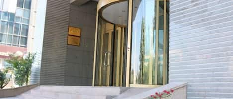 Entrada de un hotel con puerta de vidrio curva, una placa y escalones que conducen a ella.