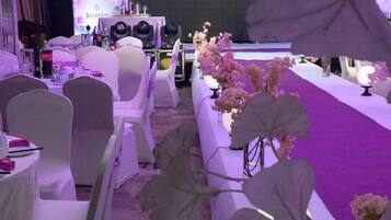 Un salón de banquetes con mesas y sillas redondas, un escenario con altavoces y una alfombra morada.