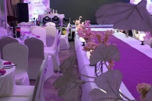 A banquet hall with round tables and chairs, a stage with speakers, and a purple carpet. - Huaxi Garden Hotel (Qingdao Liuting Airport) (Qingdao)
