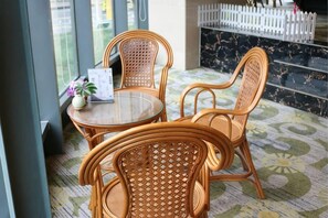Un juego de mesa y sillas de mimbre sobre un piso estampado, con una cerca blanca y vista a un edificio al fondo.