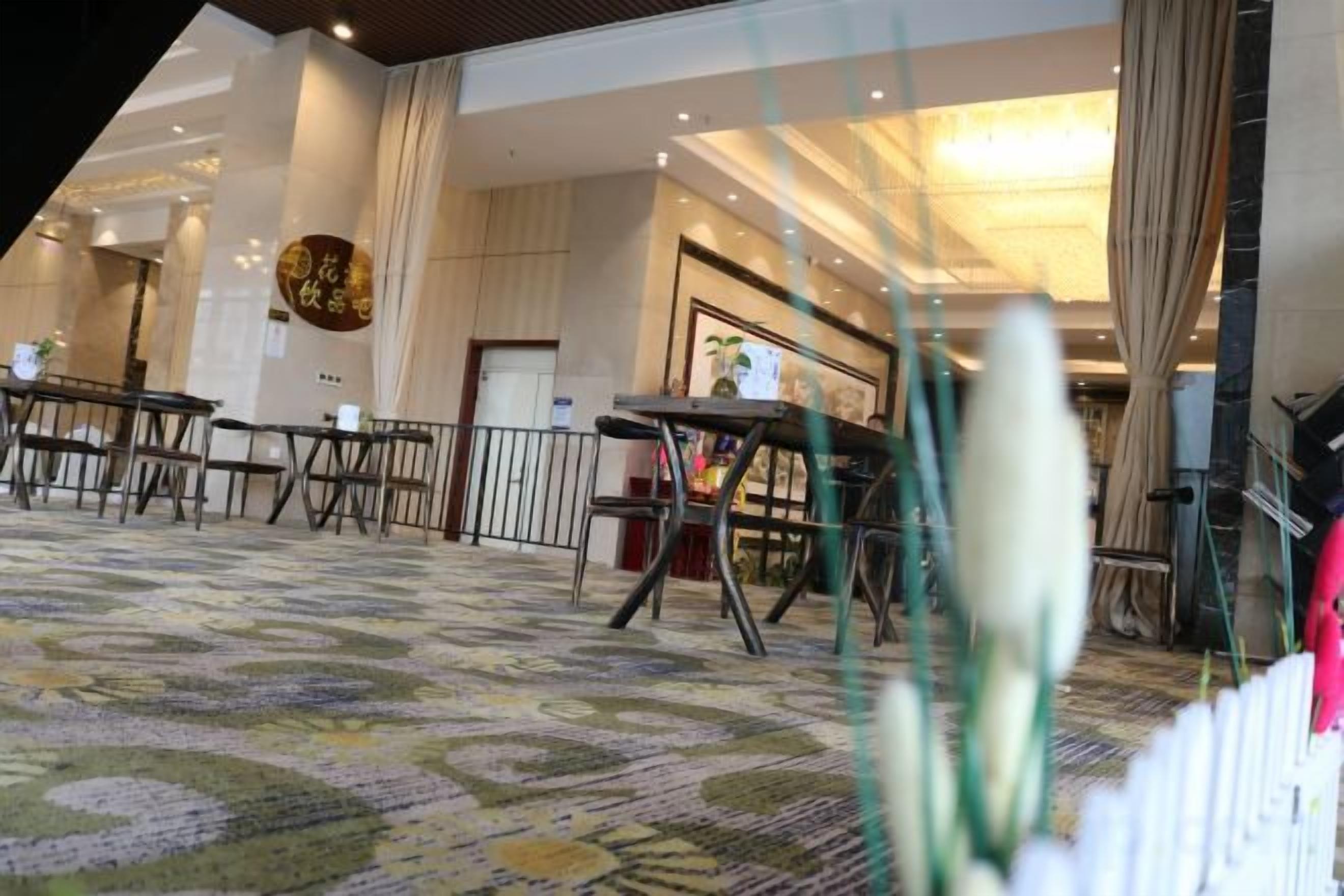 Un vestíbulo de hotel con alfombra estampada, mesas, sillas y una escalera.