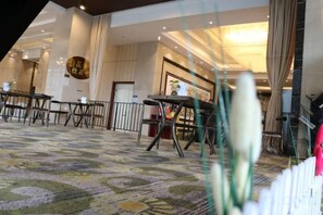 A hotel lobby with a patterned carpet, tables, chairs, and a staircase.