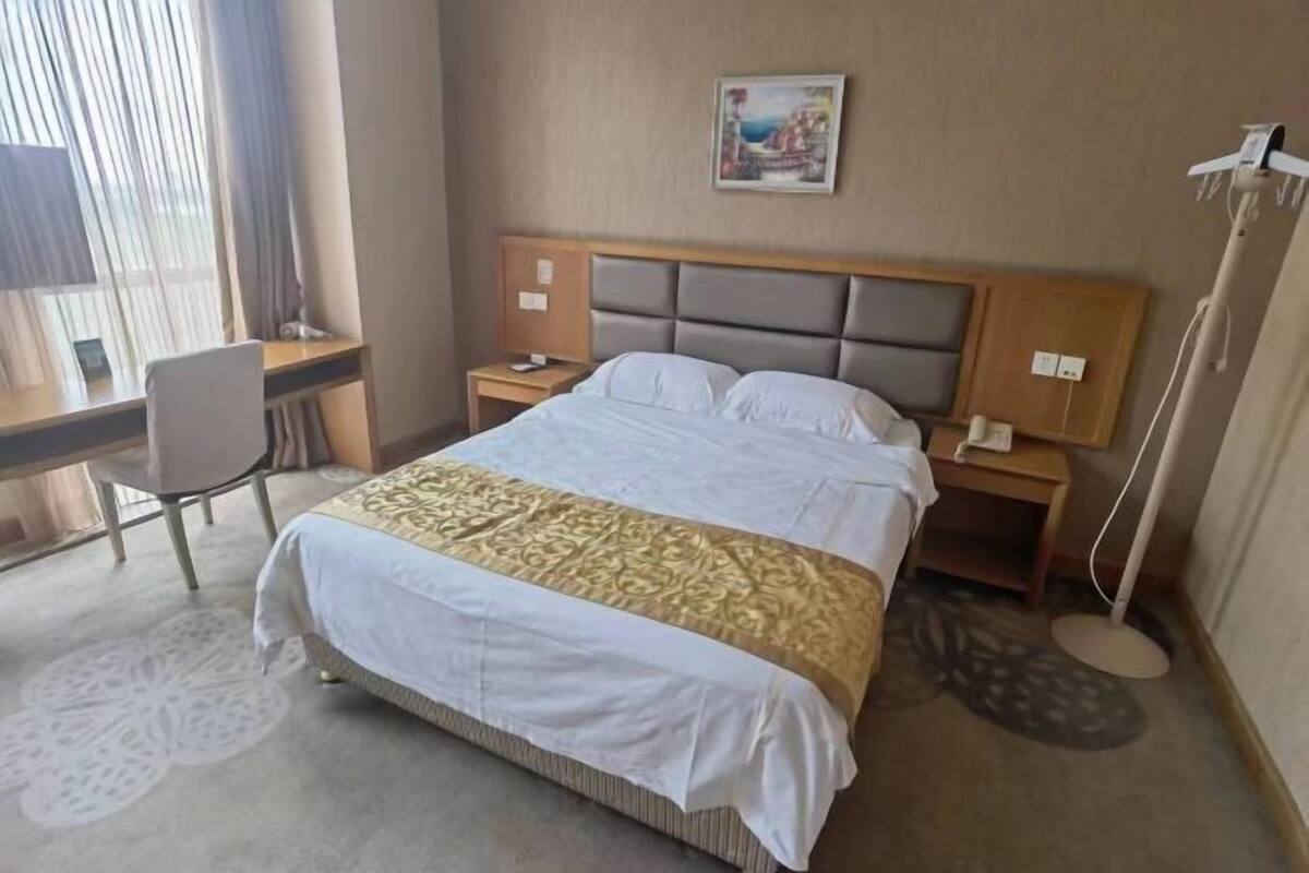 Une chambre d’hôtel comprenant un lit, un bureau, une chaise, des tables de chevet et une œuvre d’art accrochée au mur.