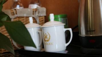 Dues tasses de ceràmica blanca amb emblemes daurats sobre un taulell, un recipient verd i una bullidora elèctrica platejada.