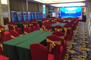 A conference room with rows of tables and chairs, a stage with a blue backdrop, and banners on the walls. - Huaxi Garden Hotel (Qingdao Liuting Airport) (Qingdao)
