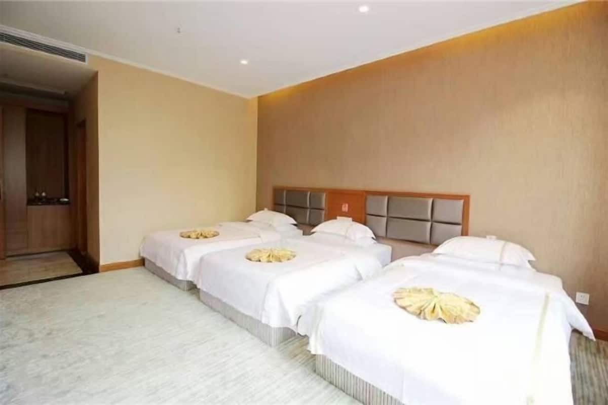 Une chambre d’hôtel avec trois lits, une tête de lit en bois et un sol recouvert de moquette.