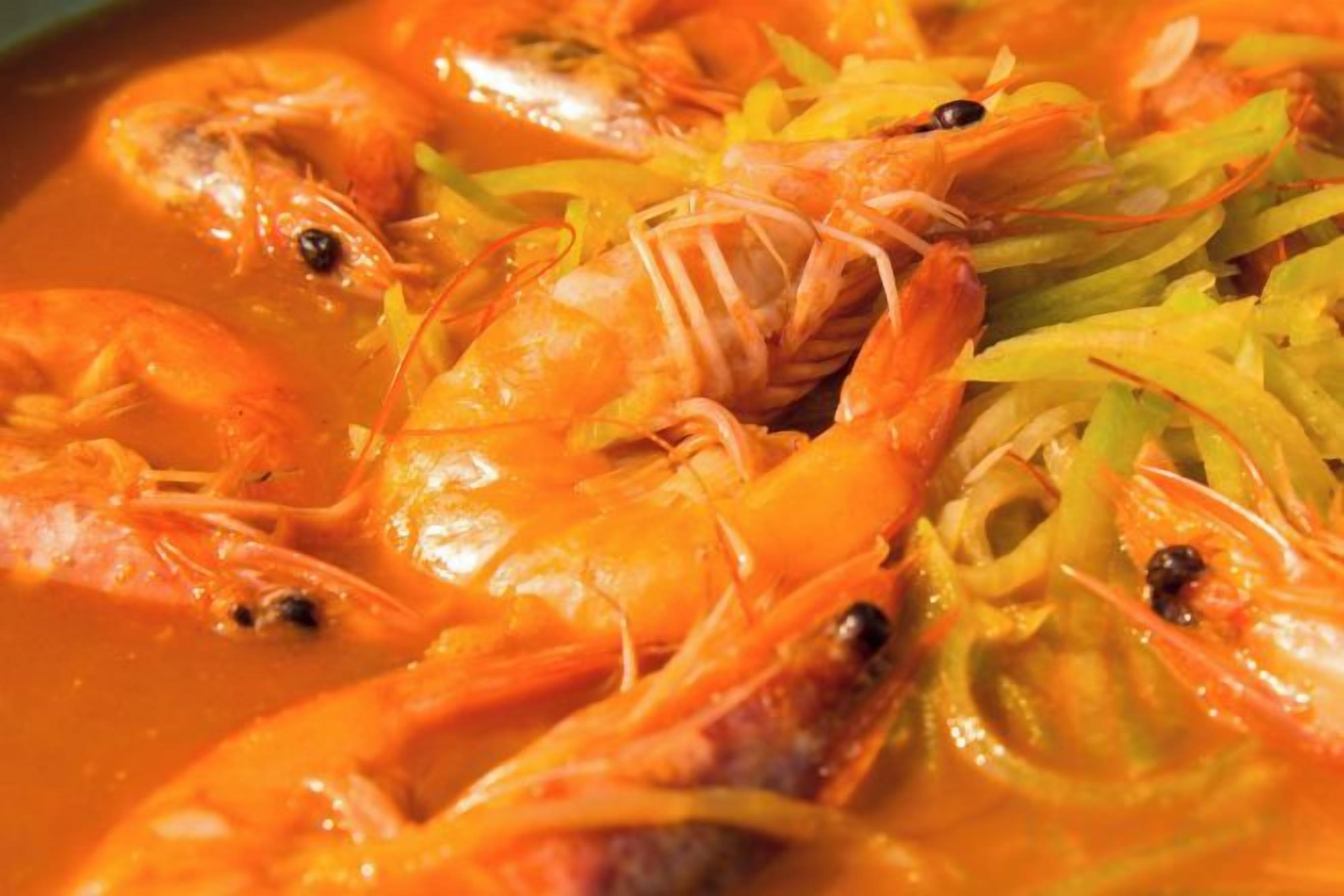 Primer plano de camarones cocidos en salsa con hierbas visibles.