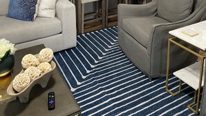 Un soggiorno moderno con un divano grigio, un tavolino in legno, un tappeto a righe blu e una poltrona grigia.
