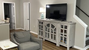 Un soggiorno con un divano grigio, una TV su un mobile bianco, un tappeto a righe e una scala.