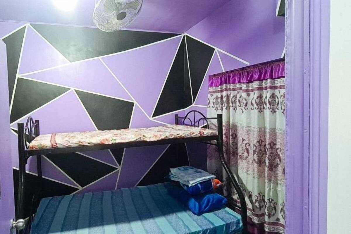 A room with a bunk bed, a fan, and a patterned curtain.