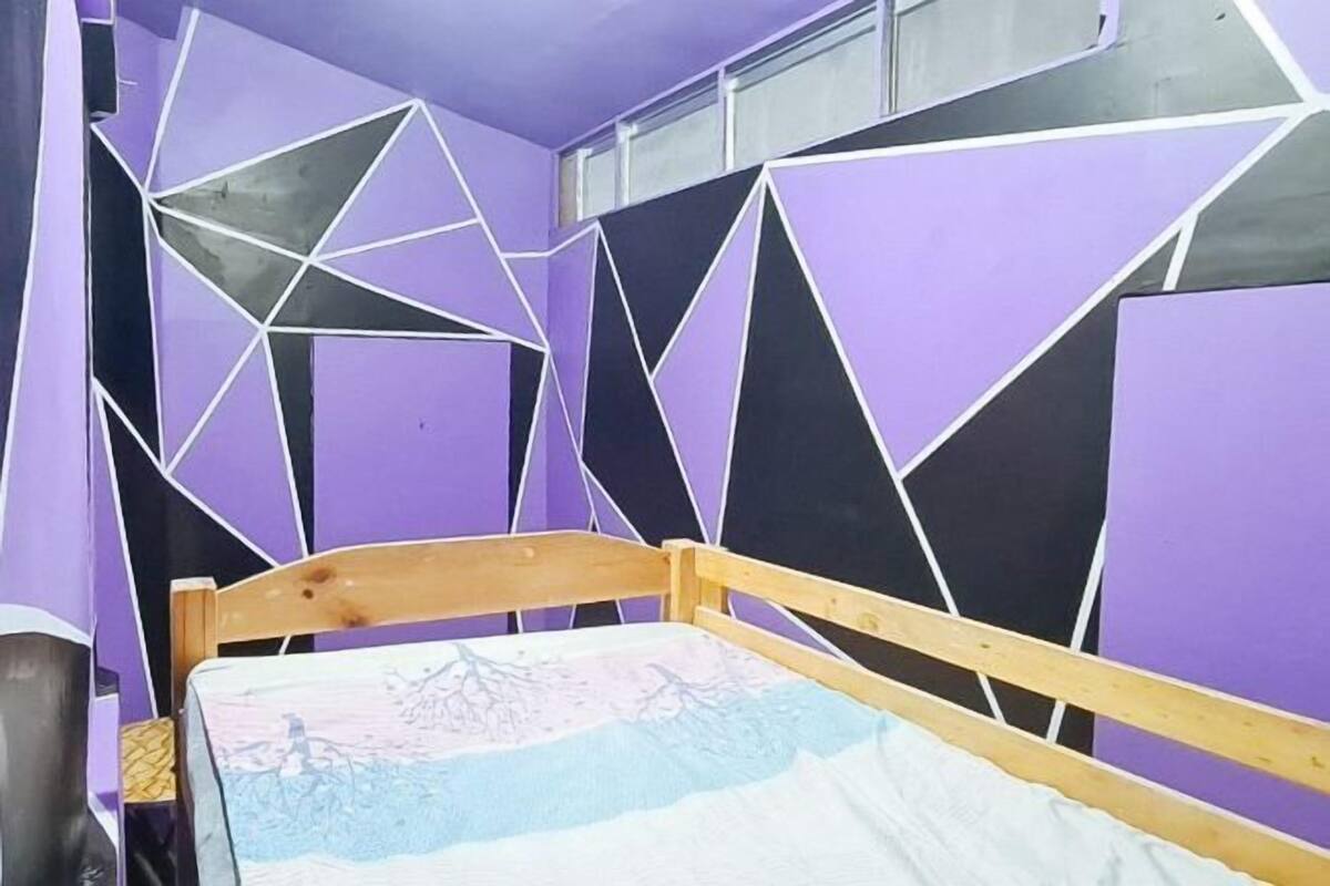 A room with a bed, purple walls, and geometric wall patterns.