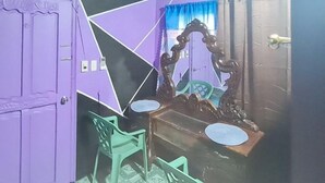 A bathroom with a purple door, a wooden vanity with a mirror, and two green plastic chairs. - Yuzons Bedspacer and Transient Home Staycation (Parañaque)