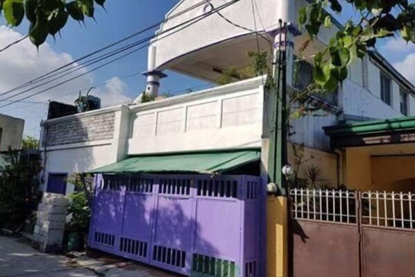 A residential building with a green awning, a purple gate, and a white exterior wall.
