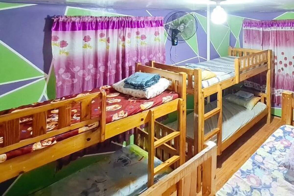A bunk bed room with a fan, curtains, and a patterned bedspread.