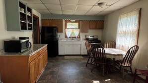 A compact kitchen with a refrigerator, stove, microwave, and wooden cabinets. - Charming 2-bedroom house in Tiona with sunset views and everything you need. (Tiona)