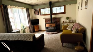 A living room with a fireplace, a sofa, a yellow armchair, and a television. - Charming 2-bedroom house in Tiona with sunset views and everything you need. (Tiona)